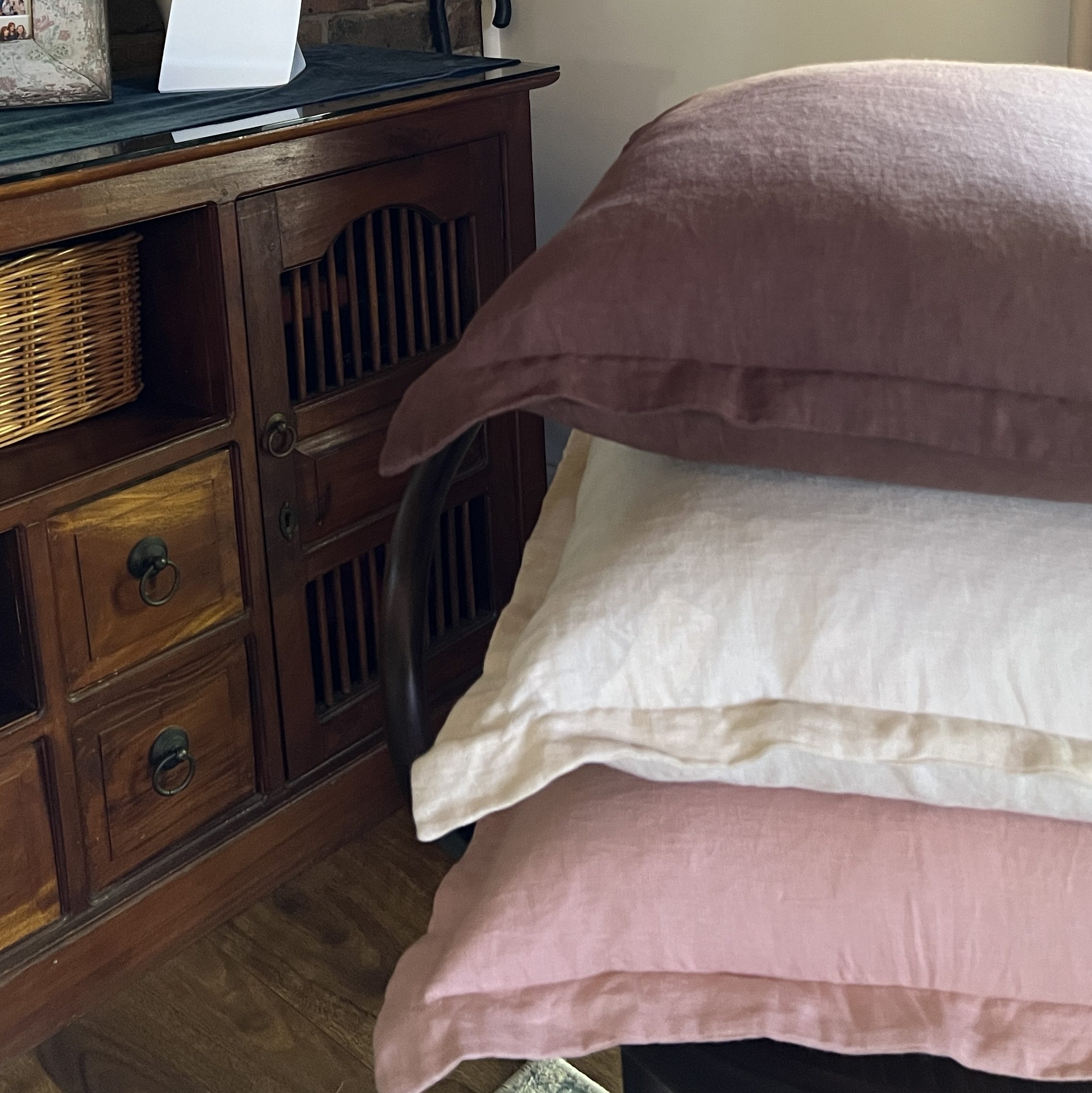 A cozy corner featuring a stack of decorative pillows in soft colors, a modern table lamp, and an art piece on the wall, against a backdrop of exposed brick and wooden furniture.